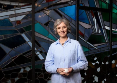 Manuela Hüttner steht vor einem bunten Kirchenfenster als Gast beim ZDF in der Sendung "die letzte Bank – Fragen an das Leben"