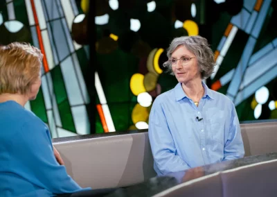 Manuela Hüttner sitzt vor einem bunten Kirchenfenster als Gast beim ZDF in der Sendung "die letzte Bank – Fragen an das Leben"